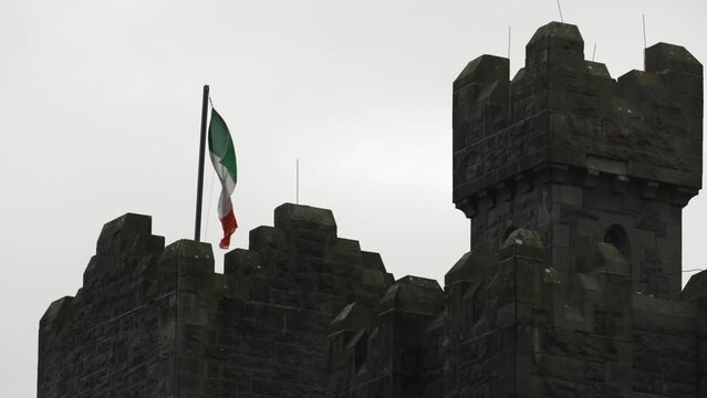 Handheld shot of an Irish flag blowing atop a castle battlement tower in Ireland
