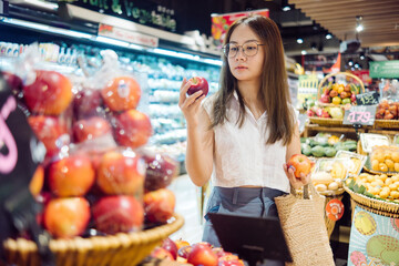 an asian woman holding for shopping an apple in a grocery store, vegan lifestyle concept.
