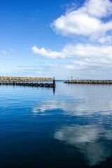 Vertical shot of a pier on a tranquil sea reflecting cloudy blue sky in Australia