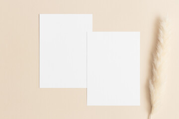 Two white invitation cards mockup with a pampas decoration on the beige table. 5x7 ratio, similar to A6, A5.