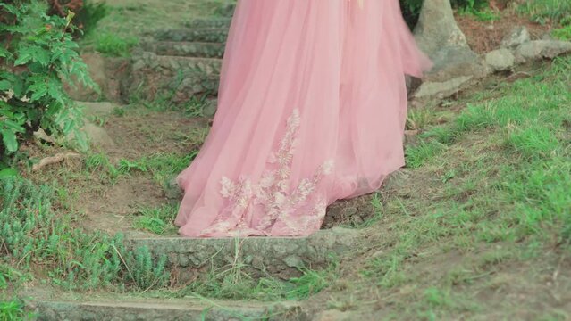Fantasy woman queen walks in green garden, climbs steps on old stone stairs medieval style. enjoys summer nature day. Girl fairy princess in pink royal silk dress back rear view long train, Lady bride