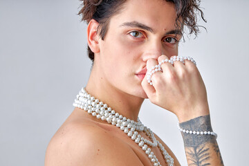 Caucasian male makeup look. portrait of shirtless young man looking posing at camera over white background. handsome gay with necklace and tattoo on hand. people, fashion, beauty concept