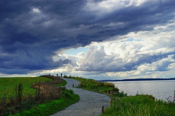 Image of a road in a field with a beautiful sky and a water surface on the right