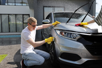 Happy young caucasian family with glove and microfiber washing or polishes car. Happiness moment of...