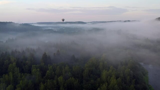 Done flight above valley filled with fog towards a hot air balloon.