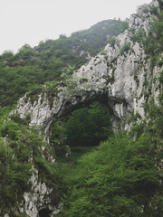 Arch of limestone with green trees all over the hills