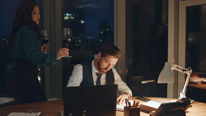 Woman bringing glass wine manager working office late evening relaxing together.