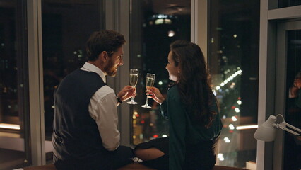 Lovely couple enjoying champagne on romantic evening date sitting at window.