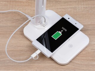 A smartphone charging on a USB lamp with a charger, the concept of technological progress