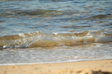 Fototapeta na wymiar Closeup shot of small waves crashing on the sand at the beach in Australia