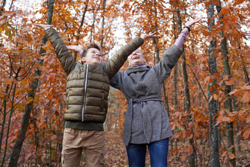 Naklejka premium A girl and a guy happily threw their hands up in the autumn forest. Happy family. Fall. Family Having Fun Outdoors. Selecrive focus