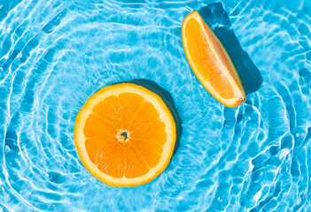 Fresh round orange slices floating in a pool with a rippled saturated blue water. Minimal tropical...