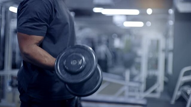 Black man performs dumbbell curls in the gym
