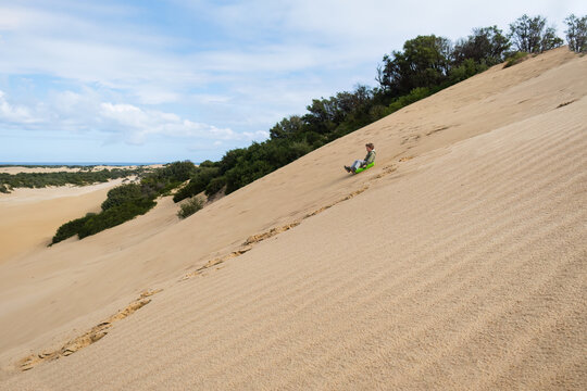 Panoramic photo of a boy sliding on toboggan from sand dunes. Sand boarding. 