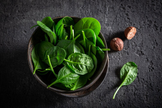 Green spinach leaves and nutmeg in dark bowl