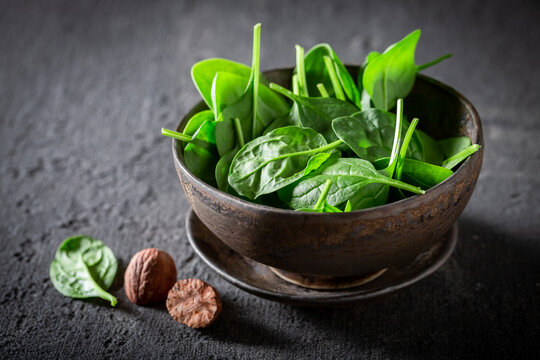 Raw green spinach leaves and nutmeg in dark bowl.