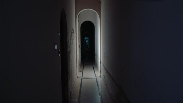 Young trendy dressed musician with guitar case walking through corridor towards the camera in old historic apartment building. Full length shot