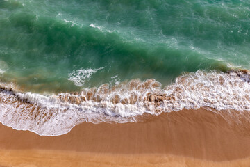 Azure sea waves hitting a sandy coast from bird eye view
