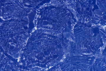 Blue water with ripples on the surface. Defocus blurred transparent blue colored clear calm water surface texture with splashes and bubbles. Water waves with shining pattern texture background.