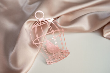 Pink paper cage with a bird on a background of pink silk draped fabric. Background picture for...