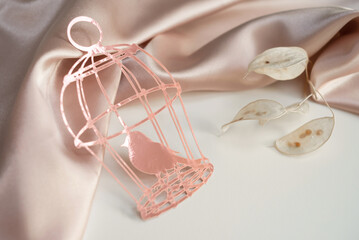 Pink paper cage with a bird on a background of pink silk draped fabric. Background picture for congratulations on the place for the inscription