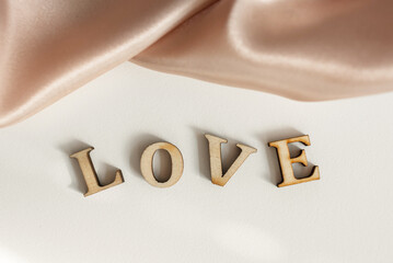 The inscription Love is made of wooden letters, on a background of pink draped silk fabric.
