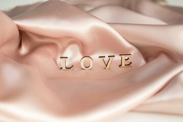 The inscription Love is made of wooden letters, on a background of pink draped silk fabric.