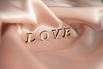 The inscription Love is made of wooden letters, on a background of pink draped silk fabric.
