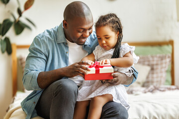 Happy Fathers day. African american baby daughter giving  gift box to dad for holiday at home  .