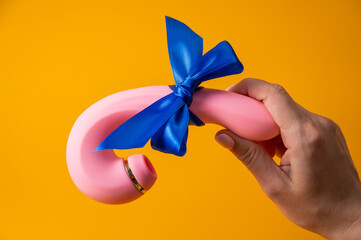 Woman holding curved pink vibrator with blue ribbon on orange background. 