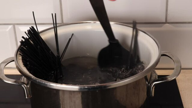 The girl cooks black pasta in a saucepan in the kitchen. cuttlefish black pasta, Stir spaghetti in a bowl