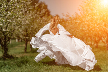 Woman white dress park. A woman in a white dress runs through a blossoming cherry orchard. The long dress flies to the sides, the bride runs rejoicing in life.