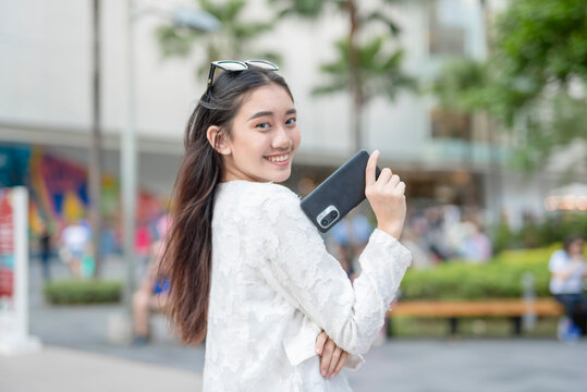 A young female asian office worker posing while proudly showing her new cellphone. Outdoor urban city setting.