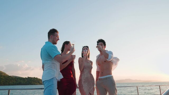 Group of young diverse people drinking wine and champagne while having sail boat party. Group of men and women friends enjoy party,having fun and talking together while yacht sailing a sunset