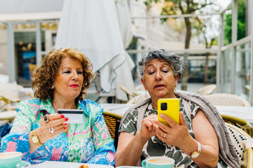Two mature women shopping online using a mobile phone outdoors