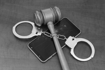 Punishing cyber crimes concept. Judge gavel and handcuffs on damaged smartphone.