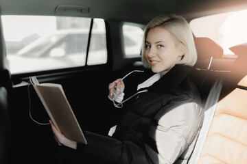 Lifestyle of modern businesswoman, blonde young woman works from car online, writes down plan in diary from taxi