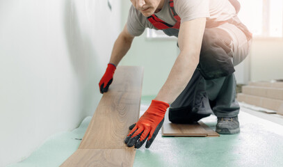 Professional worker Installing laminated or wood parquet on floor, man holding wooden tile with sun light