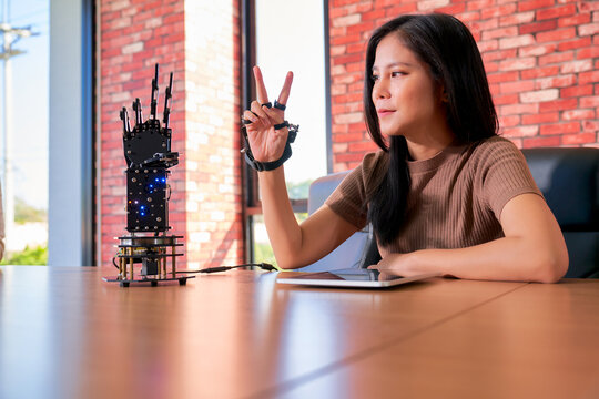 Asian woman student learning to control robotic hand controller to mirror her hand