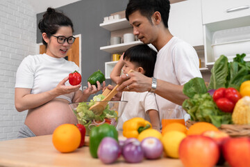 Asia pregnant mother cooking salad with husband in kitchen at home	