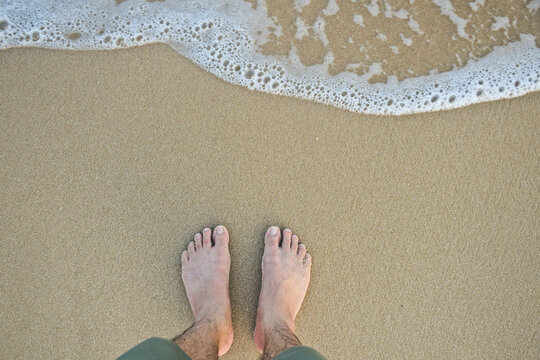 feet with wave on sandy beach top view