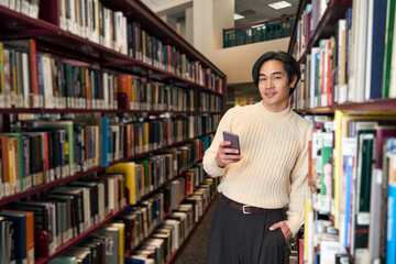 Fototapeta na wymiar Portrait of smart Japanese university student holding mobile phone in bookstore