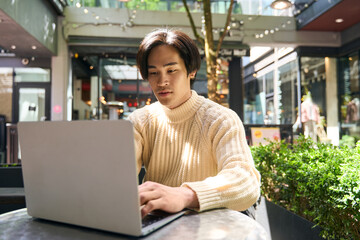 Confident asian man author typing laptop computer keyboard, sitting outdoor cafe