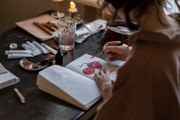 Creative hobbies. Close up of female artist sitting at table with burning candles painting in...