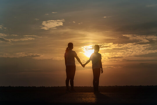 Silhouette of happy family mother and daughter holding hands on sunset background, holiday freedom lifestyle