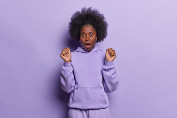 Indoor shot of young Afro woman has stunned and shocked look gasps from something horrible keeps...