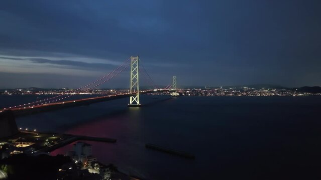 Car lights on span of long suspension bridge to city in twilight