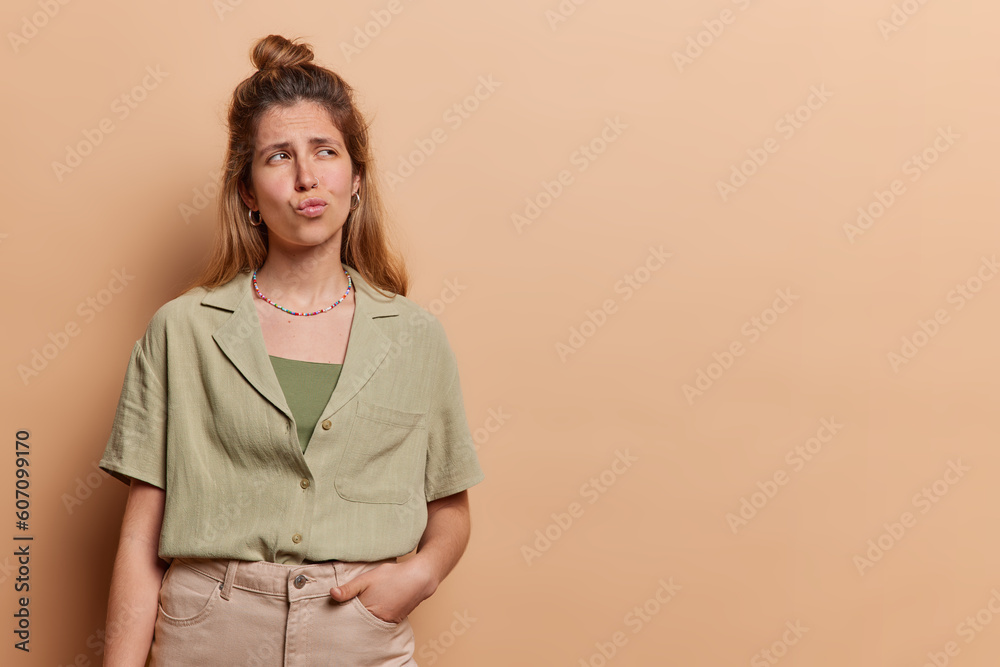 Wall mural horizontal shot of thoughtful european woman ponders on something keeps hand in pocket of trousers h