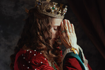 medieval queen in red dress with rosary and crown praying