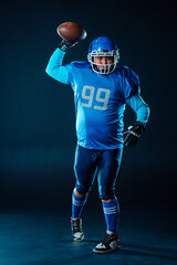 Fototapeta na wymiar Portrait of a man in a blue uniform for american football throws the ball on a black background. 